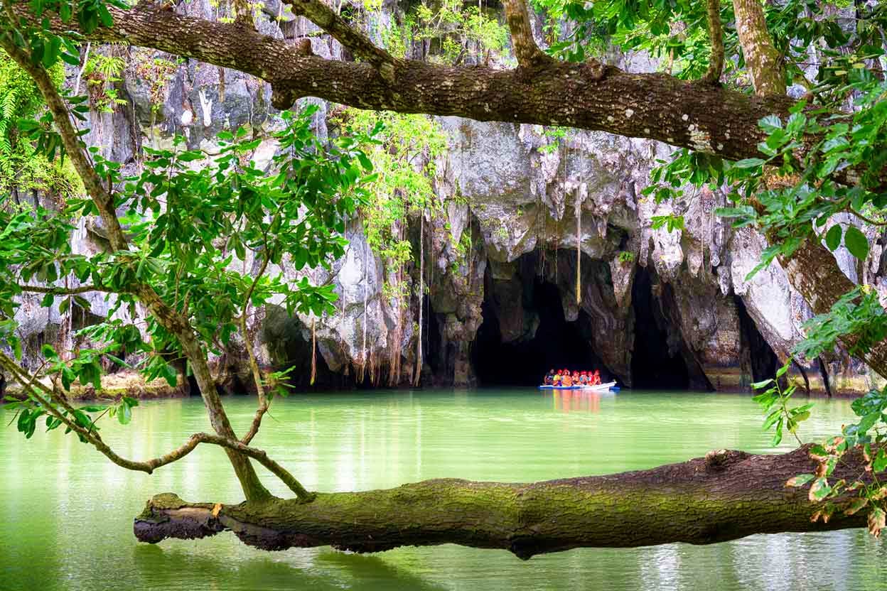 Philippines Visa Tourist boat with passengers on emerald lagoon surrounded by limestone cliffs and lush vegetation in Philippines cave